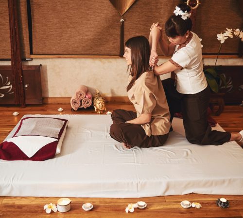 Asian woman wearing flower hair tie bringing client right arm behind her head during muscle massage